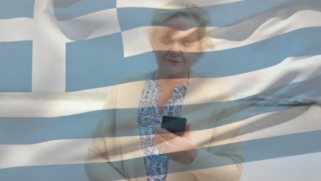 Animation-of-flag-of-greece-over-happy-senior-caucasian-woman-using-smartphone-on-beach