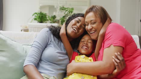 Happy-african-american-grandmother,-mother-and-daughter-hugging-on-sofa