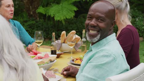Animation-of-happy-african-american-senior-man-eating-lunch-in-garden-with-friends