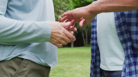 Animation-of-midsection-of-caucasian-female-and-male-senior-friends-holding-hands-in-garden