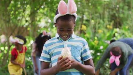 Animation-of-happy-african-american-boy-holding-easter-egg-in-garden