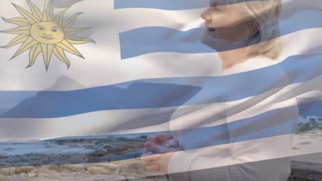 Animación-De-La-Bandera-De-Uruguay-Sobre-Una-Feliz-Mujer-Caucásica-Mayor-En-La-Playa