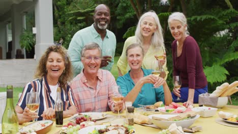 Animation-of-diverse-happy-senior-female-and-male-friends-eating-lunch-in-garden