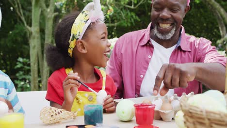 Animation-of-happy-african-american-grandfather-and-grandchildren-painting-easter-eggs-in-garden