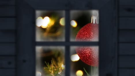 Animation-of-snow-falling-over-christmas-tree-and-red-bauble-seen-through-window