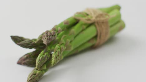 Video-of-close-up-of-bundle-of-fresh-asparagus-over-white-background
