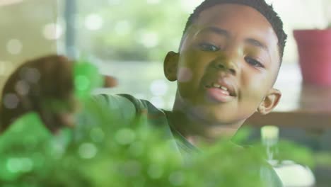 Animation-Von-Lichtern-Auf-Dem-Wasser-über-Einem-Glücklichen-Afroamerikanischen-Jungen,-Der-Zimmerpflanzen-Gießt