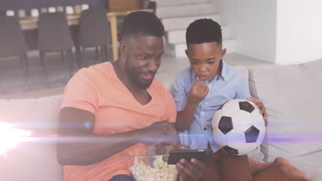 Animation-Von-Lichtern-über-Einem-Glücklichen-Afroamerikanischen-Vater-Und-Sohn,-Die-Sich-Ein-Fußballspiel-Auf-Dem-Smartphone-Ansehen