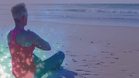 Animation-of-light-spots-over-caucasian-woman-practicing-yoga-and-meditating-at-beach