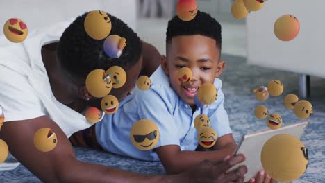Animation-of-emoticons-over-happy-african-american-father-and-son-using-tablet