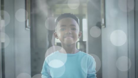 Animation-of-bokeh-over-happy-african-american-boy-standing-in-hall