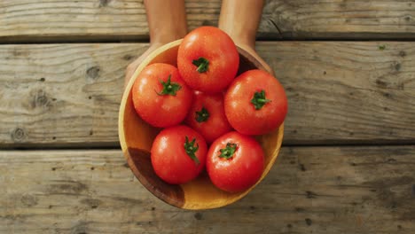 Video-of-biracial-man-holding-bowl-of-fresh-red-tomatoes-on-wooden-background