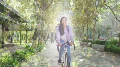 Animation-of-leaves-over-smiling-asian-woman-cycling