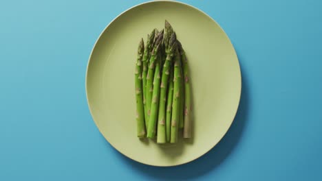 Video-of-fresh-asparagus-on-green-plate-over-blue-background