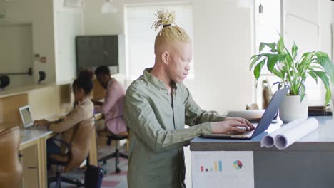Portrait-of-happy-albino-african-american-businessman-using-laptop-in-creative-office