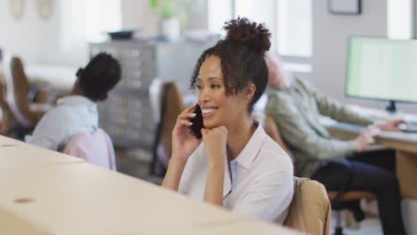 Happy-african-american-businesswoman-talking-on-smartphone-in-creative-office