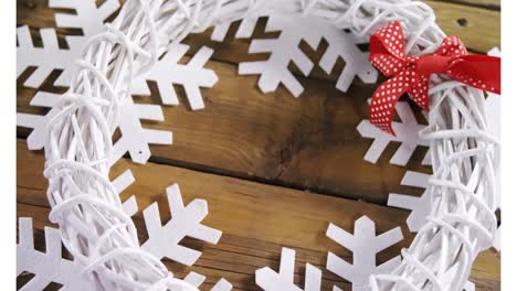 Animation-of-white-crown-and-snowflakes-shapes-on-wooden-table-at-christmas