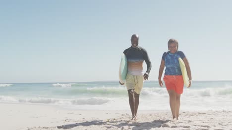Glückliches-älteres-Afroamerikanisches-Paar,-Das-Mit-Surfbrettern-Am-Sonnigen-Strand-Spaziert