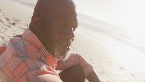 Senior-african-american-man-wearing-shirt-and-sitting-on-sunny-beach