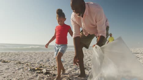 Senior-african-american-couple-with-grandchildren-segregating-waste-on-sunny-beach