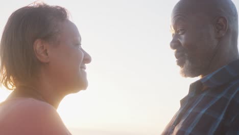 Smiling-senior-african-american-couple-looking-at-each-other-on-sunny-beach