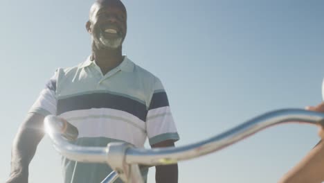 Sonriente-Pareja-Afroamericana-Senior-Caminando-Con-Bicicletas-En-La-Playa-Soleada