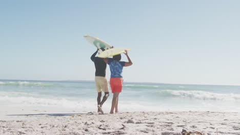 Senior-african-american-couple-walking-with-surfboards-on-sunny-beach