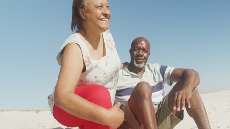 Smiling-senior-african-american-couple-embracing-and-looking-at-sea-on-sunny-beach