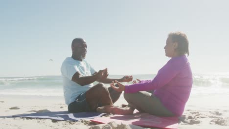 Älteres-Afroamerikanisches-Paar,-Das-Yoga-Praktiziert-Und-Am-Sonnigen-Strand-Meditiert