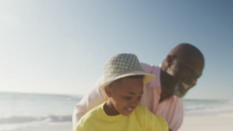 Lächelnder-älterer-Afroamerikanischer-Mann-Mit-Enkel,-Der-Am-Sonnigen-Strand-Spielt
