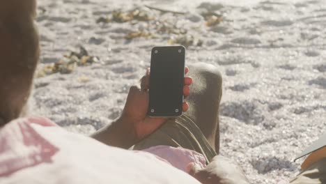 Senior-african-american-man-lying-on-sunbed-and-using-smartphone-on-sunny-beach