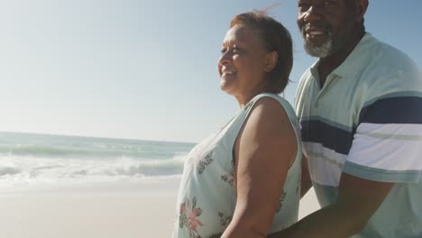 Portrait-of-smiling-senior-african-american-couple-embracing-on-sunny-beach