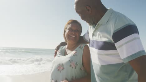Sonriente-Pareja-Afroamericana-Senior-Abrazándose-Y-Caminando-En-La-Playa-Soleada