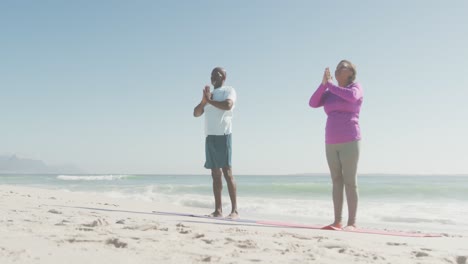 Senior-african-american-couple-practicing-yoga-on-mats-on-sunny-beach