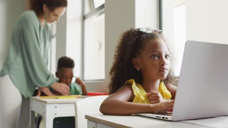 Video-of-focused-african-american-girl-sitting-at-desk-with-laptop-during-lesson-in-classroom