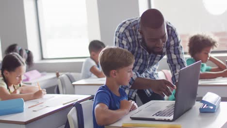 Video-of-happy-african-american-male-teacher-helping-caucasian-boy-with-laptop