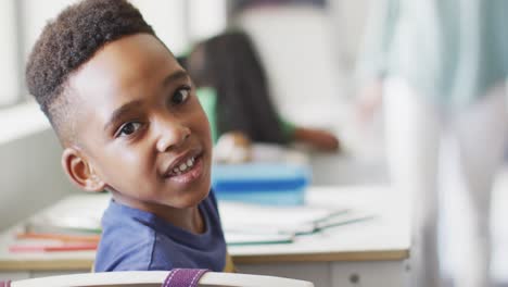 Video-of-happy-african-american-boy-sitting-at-desk-during-lesson-in-classroom