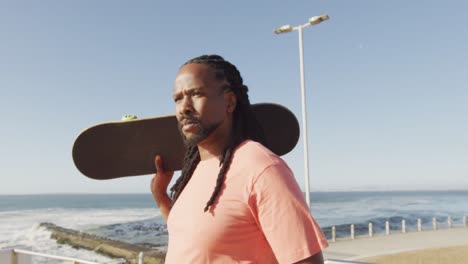Video-of-african-american-man-holding-skateboard-by-sea