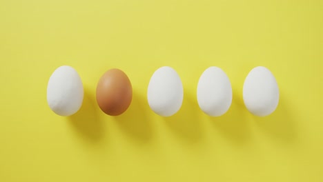Video-of-row-of-one-brown-and-four-white-eggs-with-copy-space-on-yellow-background
