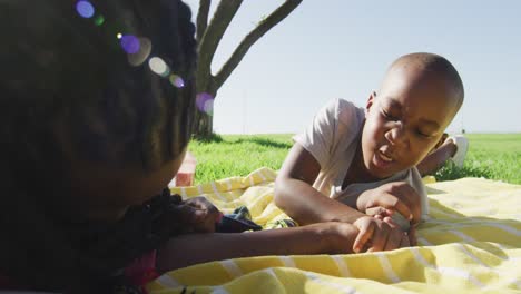 Video-of-happy-african-american-father-and-son-having-picnic-on-grass,-arm-wrestling