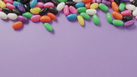 Video-of-close-up-of-multi-coloured-sweets-with-copy-space-over-purple-background