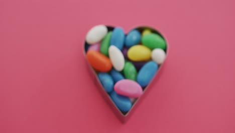 Video-of-overhead-view-of-multi-coloured-sweets-in-heart-shape-over-red-background