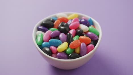 Video-of-close-up-of-multi-coloured-sweets-in-bowl-over-purple-background