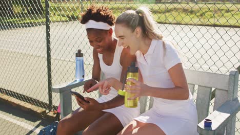 Video-of-happy-diverse-female-tennis-players-sitting,-talking-and-resting-after-match