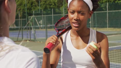 Video-of-happy-african-american-female-tennis-player-holding-racket-and-talking-with-friend