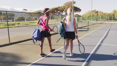 Video-of-back-of-diverse-female-tennis-players-holding-racket,-walking-and-talking