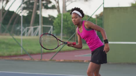 Video-of-focused-african-american-female-tennis-player-holding-racket-and-hitting-ball