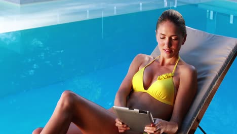 Wunderschöne-Blondine-Im-Bikini,-Die-Mit-Einem-Tablet-PC-Auf-Einem-Liegestuhl-Am-Pool-Liegt