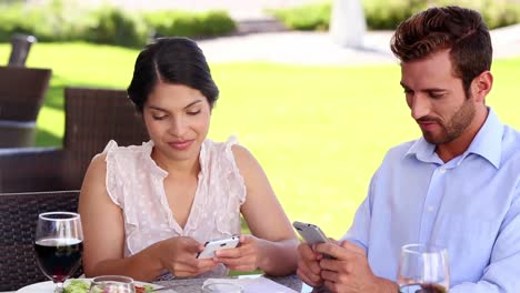 Ein-Paar-Schreibt-Beim-Mittagessen-SMS-Auf-Seinen-Handys