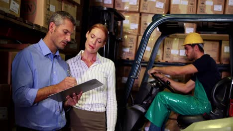 Warehouse-management-talking-with-forklift-driver-behind